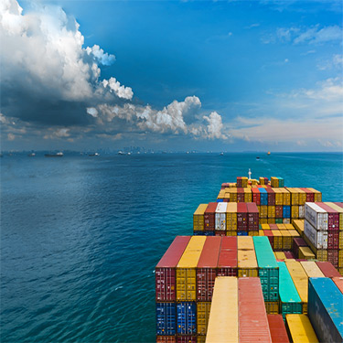 Shipping carrier deck with containers of different colors on top and ocean in the background